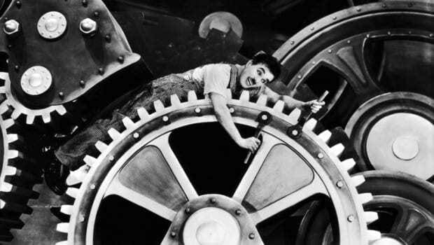Cena do Filme Tempos Modernos, de Charles Chaplin. Ator deitado em engrenagem ajustando parafusos do maquinário.